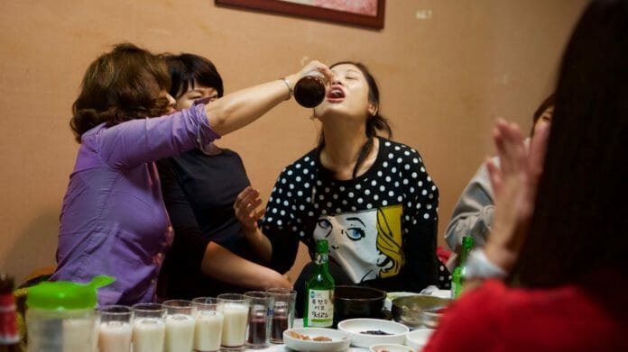 Trong một bữa tiệc rượu, một người phụ nữ đang rót chai rượu vào miệng một người phụ nữ khác.
