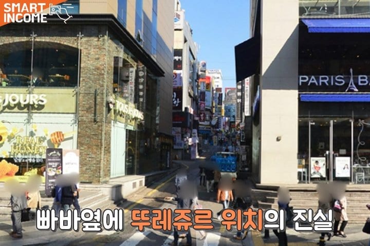 Một con phố mua sắm sầm uất ở Hàn Quốc với cửa hàng của Paris Baguette ở bên phải và cửa hàng của Tous les Jours bên trái.