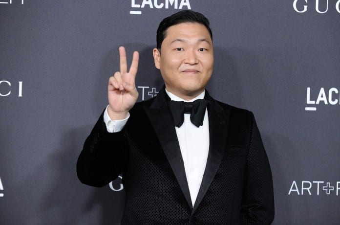 Ca sĩ Psy giơ tay chữ V tạo hình chụp ảnh trong một sự kiện.