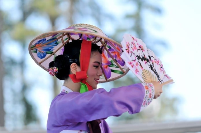 Cô gái trong trang phục gisaeng hanbok, đầu đội nón và đang múa quạt giấy.
