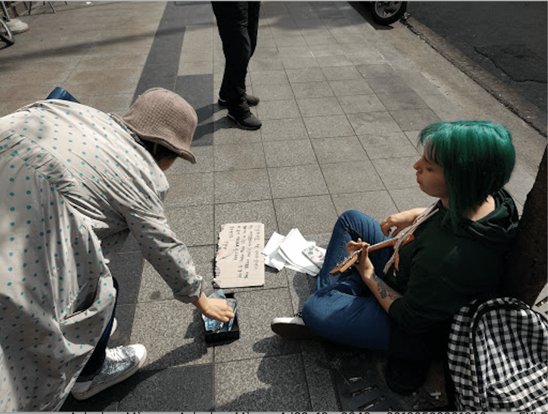 Một bà cụ Hàn Quốc đang cúi người cho đồng xu một nữ du khách Tây ba lô có mái tóc màu xanh.